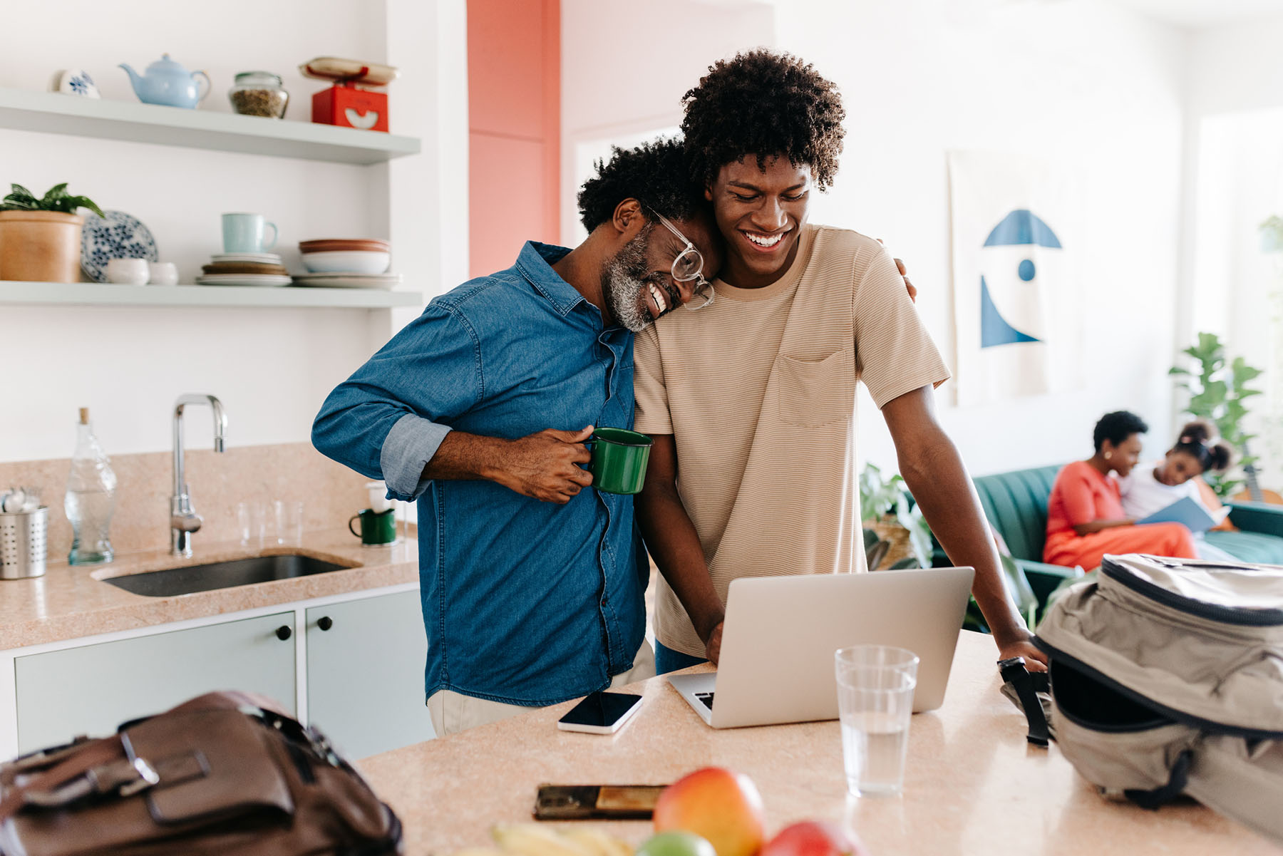 Father and teenage son smiling in the kitchen with laptop, highlighting family connection and parent-teen relationship support through therapy