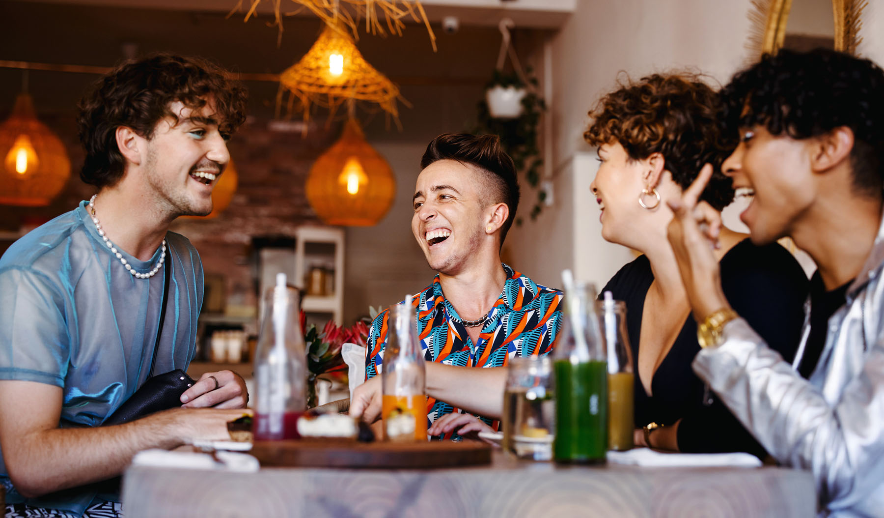 Group of LGBTQ+ individuals laughing at a café table, illustrating community, belonging, and the importance of inclusive mental health support in affirming spaces.