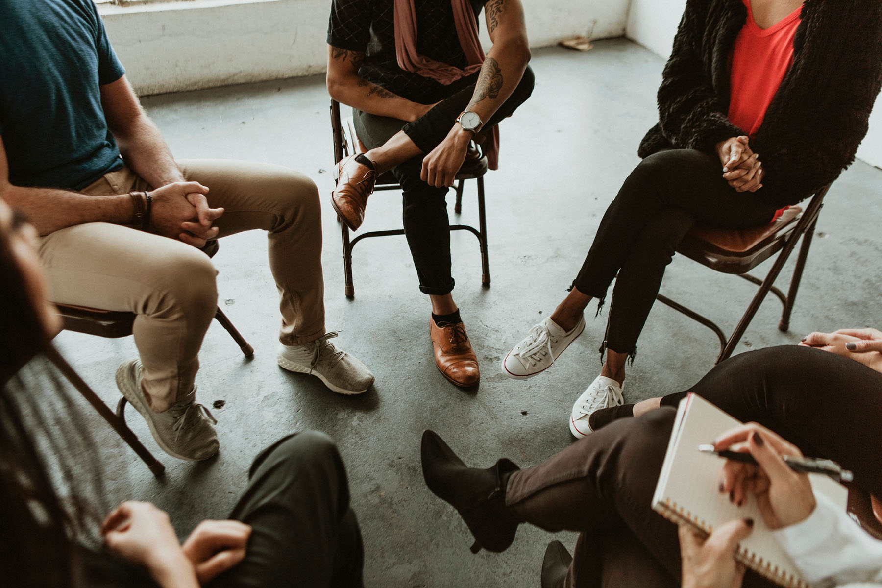 Circle of people sitting in chairs during group therapy, representing safe, supportive spaces for recovery and shared experiences