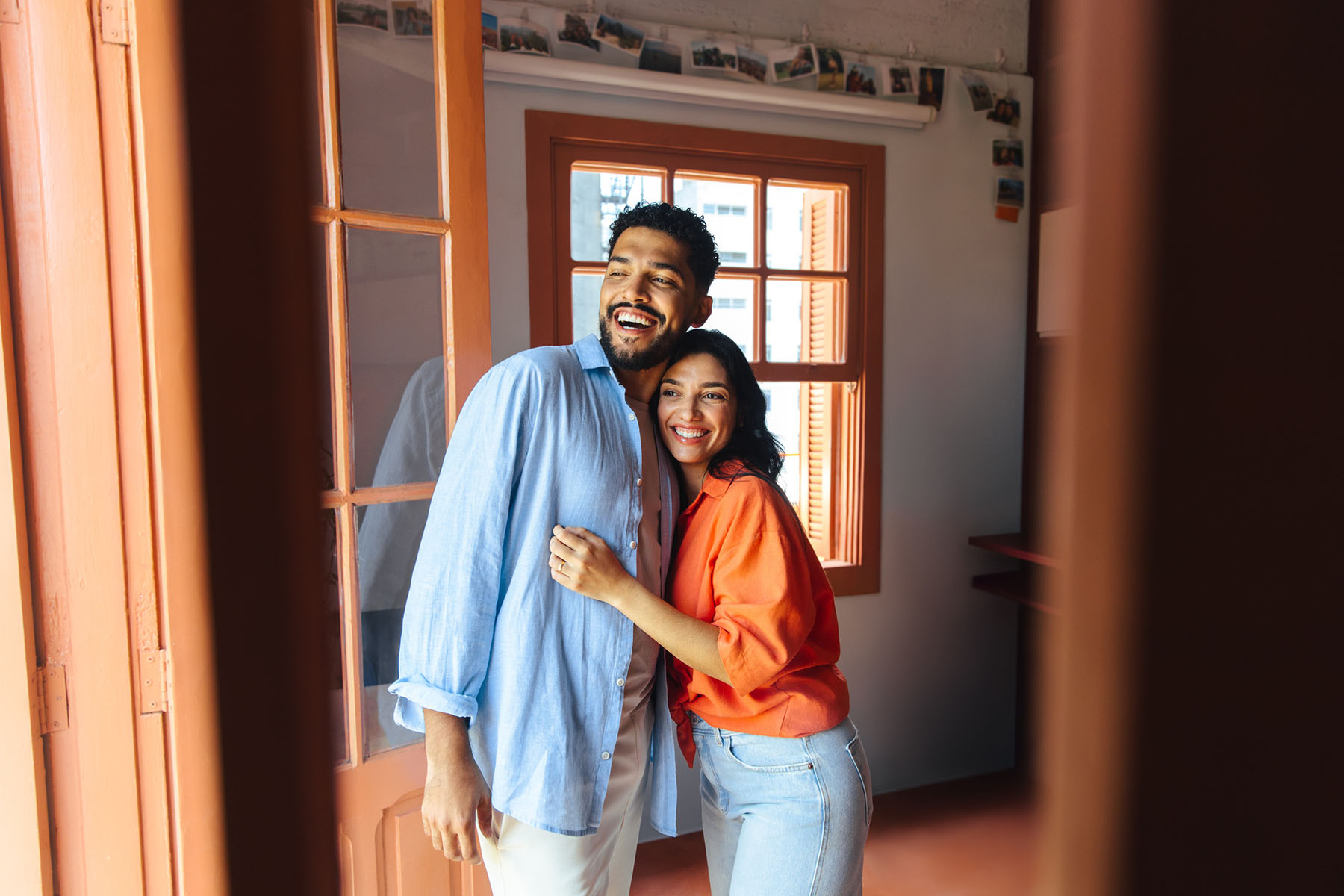 Young couple embracing and laughing near a bright window, representing growth, healing, and connection through relationship therapy