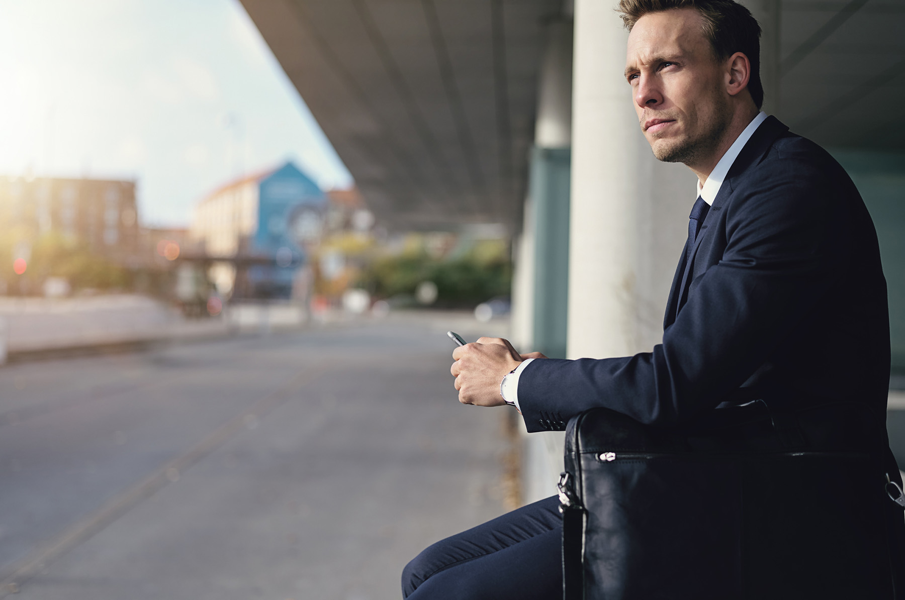 Man in a suit sitting thoughtfully at a city bus stop with a phone, conveying stress management, decision-making support, and the relevance of counseling for working professionals.